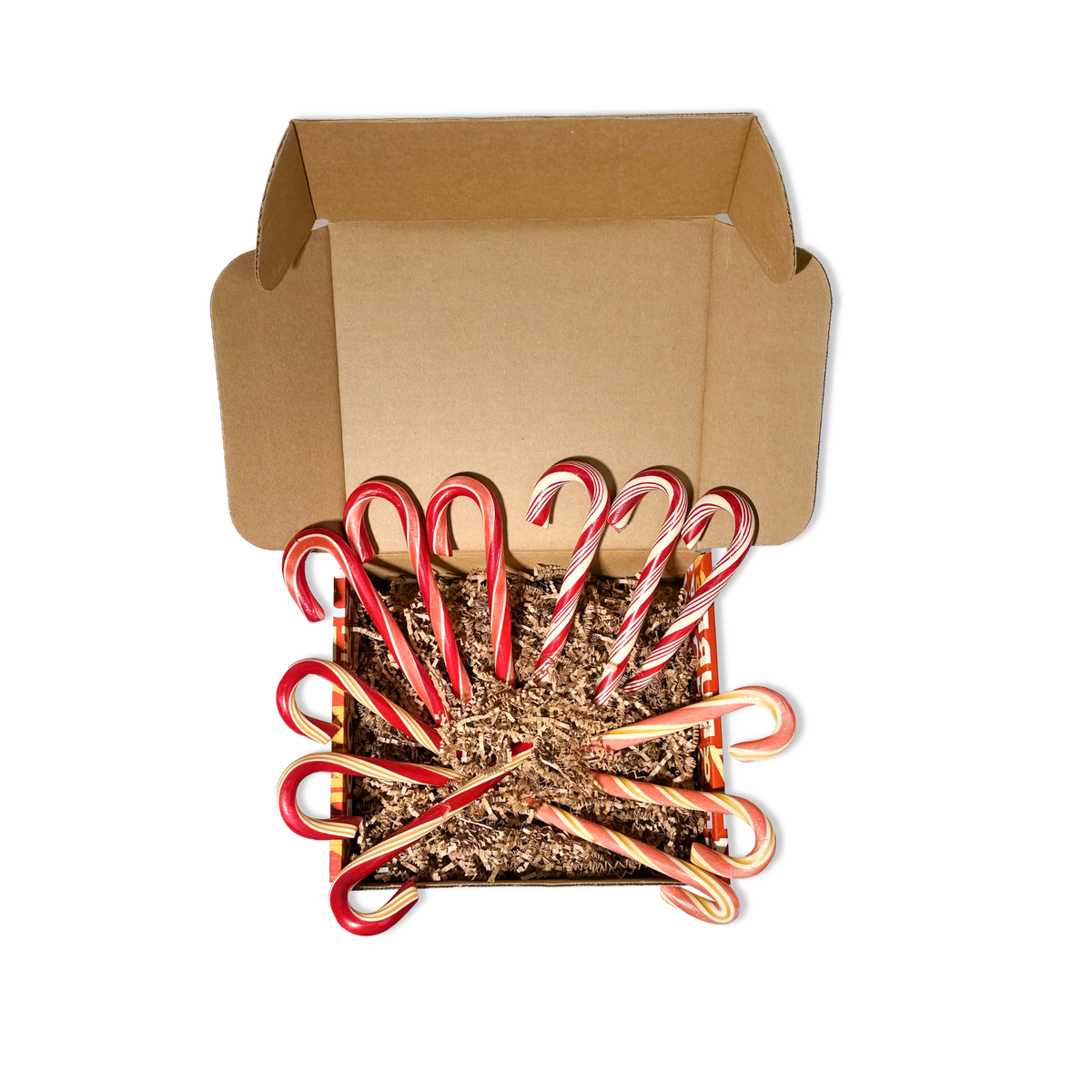 A set of red and white striped candy canes arranged in a fan shape inside a brown kraft paper gift box filled with shredded paper, on a white background.