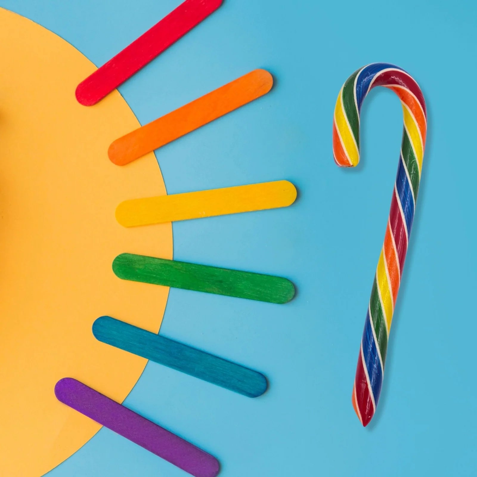 Colorful candy cane and popsicle sticks and yellow paper in shape of a sun on a blue background