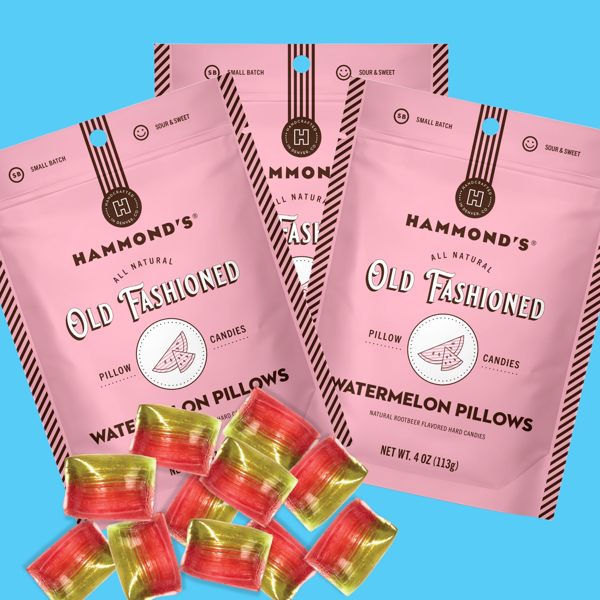 Three pink bags of Hammond's Old Fashioned Watermelon Pillow candies are arranged on a bright blue background, with several individually wrapped red and yellow candies placed in front.